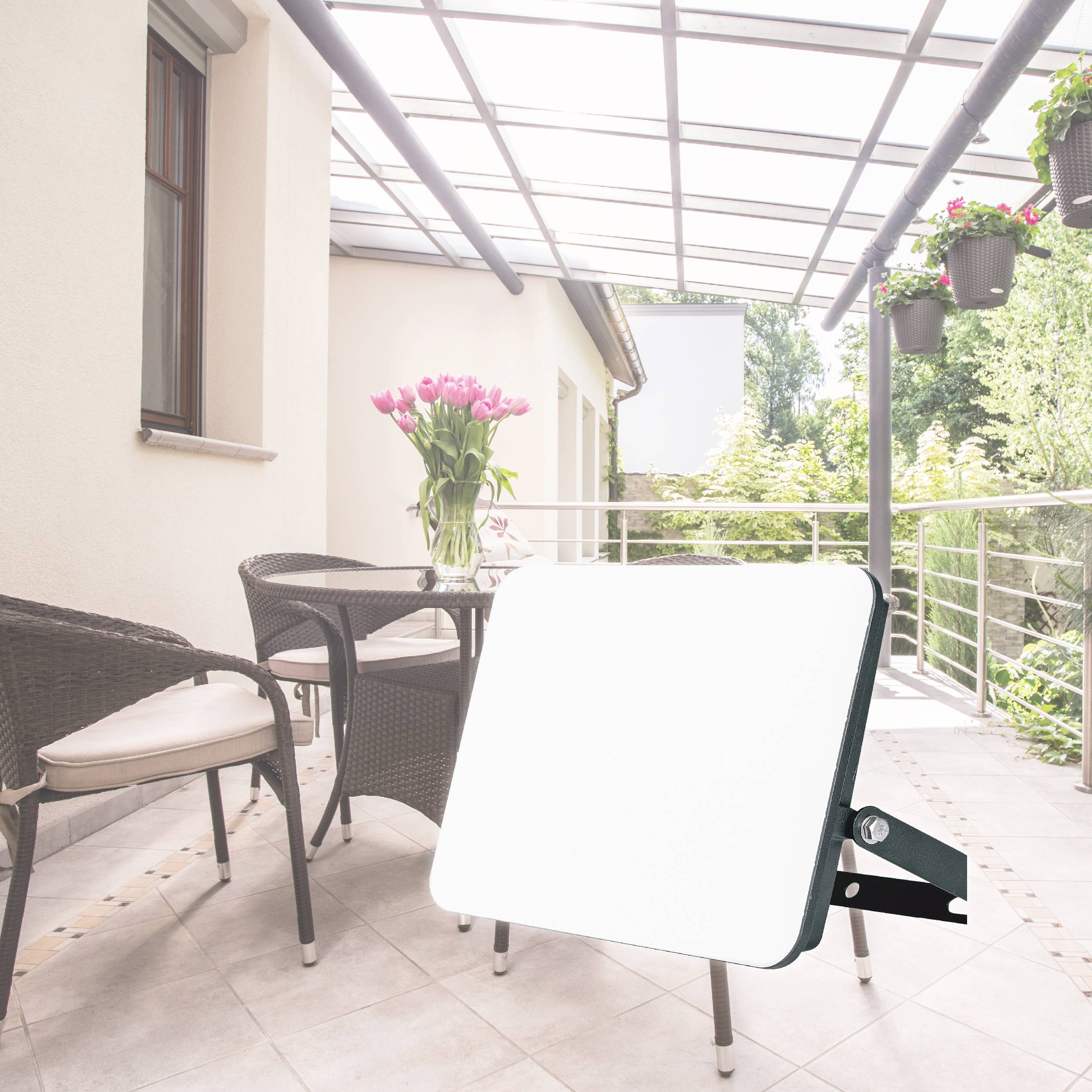 A bright LED floodlight is positioned on a covered terrace, surrounded by potted plants, chairs, and a table.
