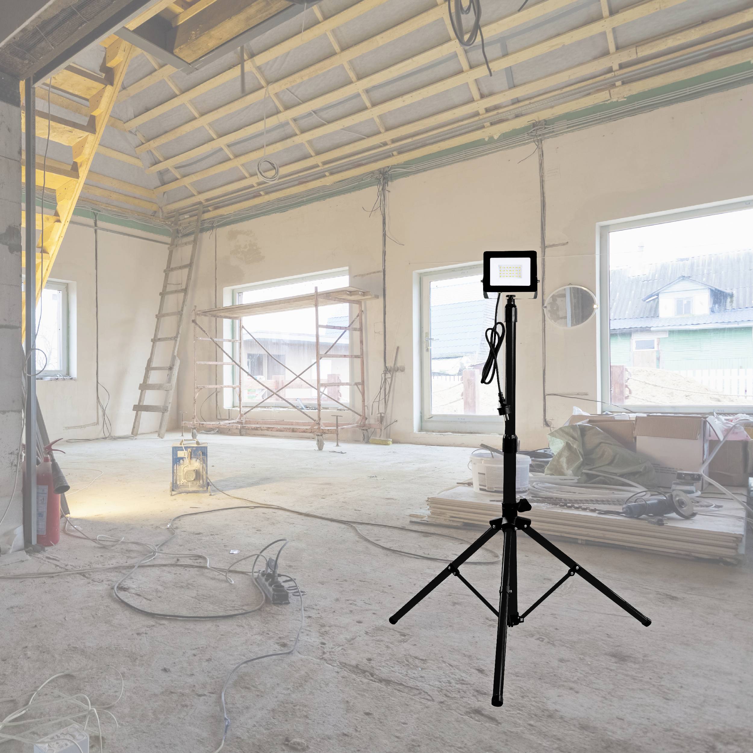A construction site in an unfinished room with three windows. In the foreground, a tripod with a mounted construction spotlight stands. Tools and materials are scattered around.
