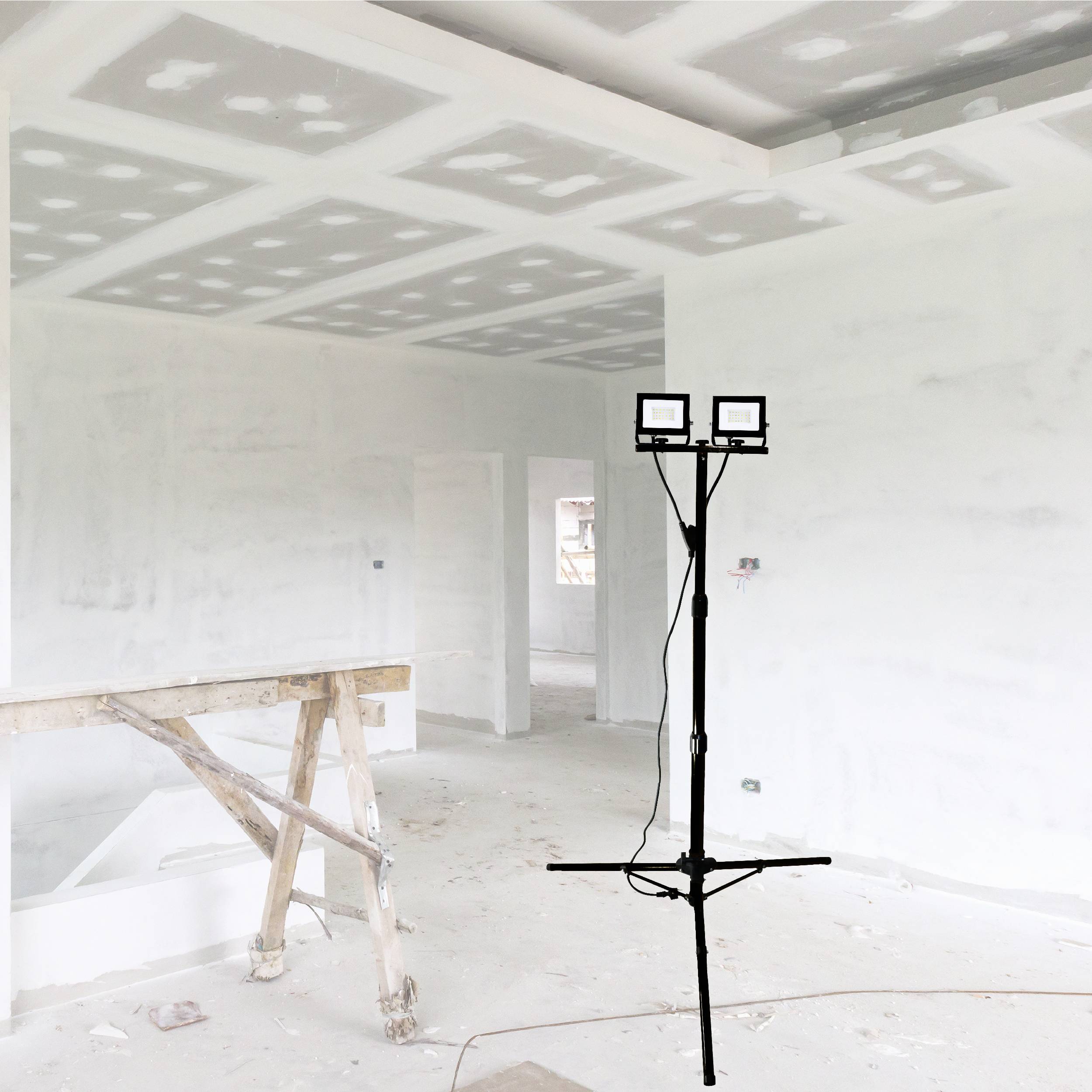 A partially completed room with white plasterboard walls and ceiling, two ceiling lights mounted on a stand, dusty floor, construction environment.