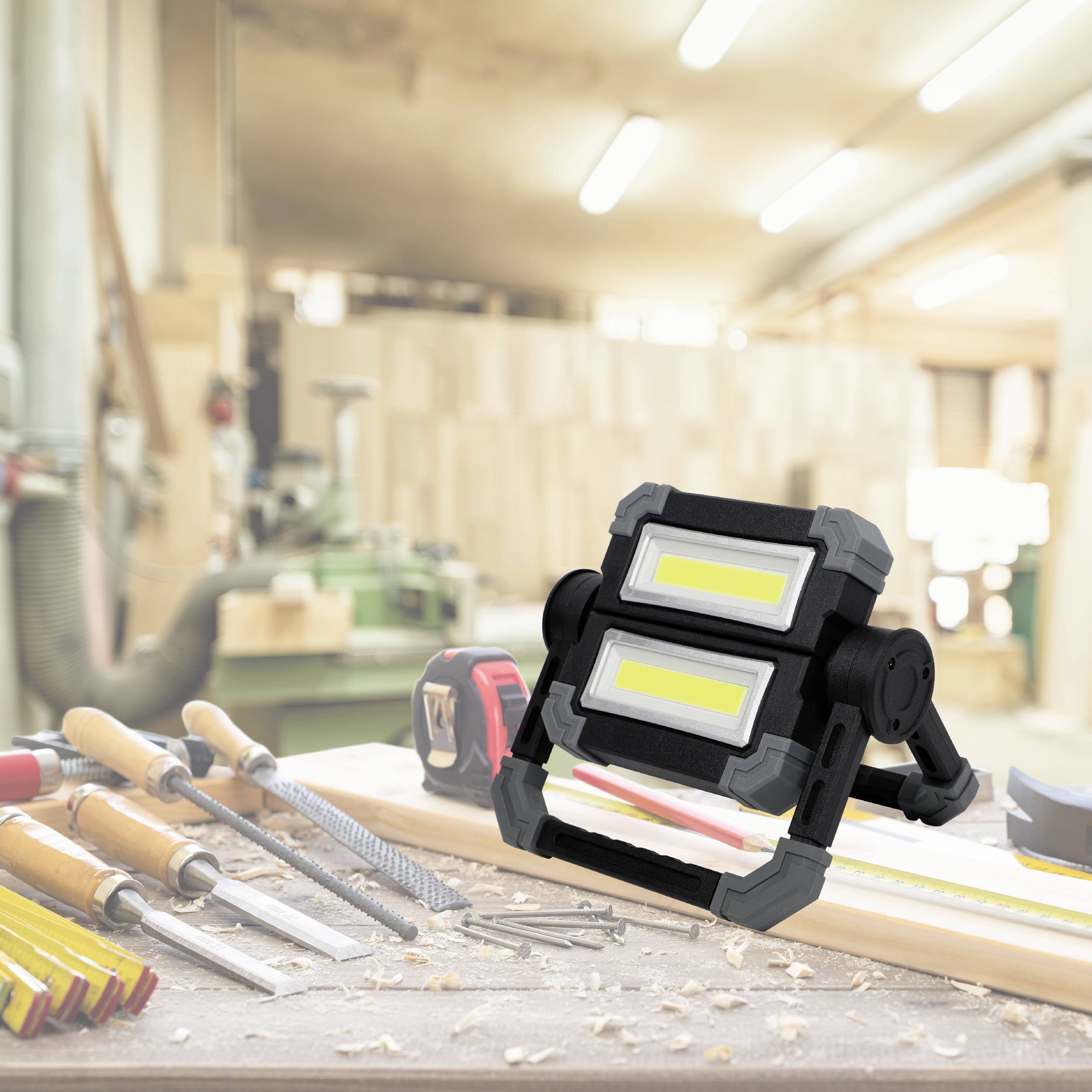 A workshop with tools on a workbench and a bright LED work light in the foreground. Background out of focus.