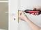 A person uses a red and black cordless screwdriver to install or remove a screw from a door handle on a white door.
