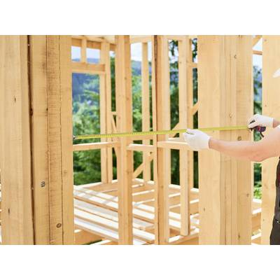 Person measuring a wooden frame structure with a tape measure, outdoors.