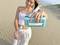 A woman on a sandy beach is pouring water from a bottle into a water container with an integrated filter.