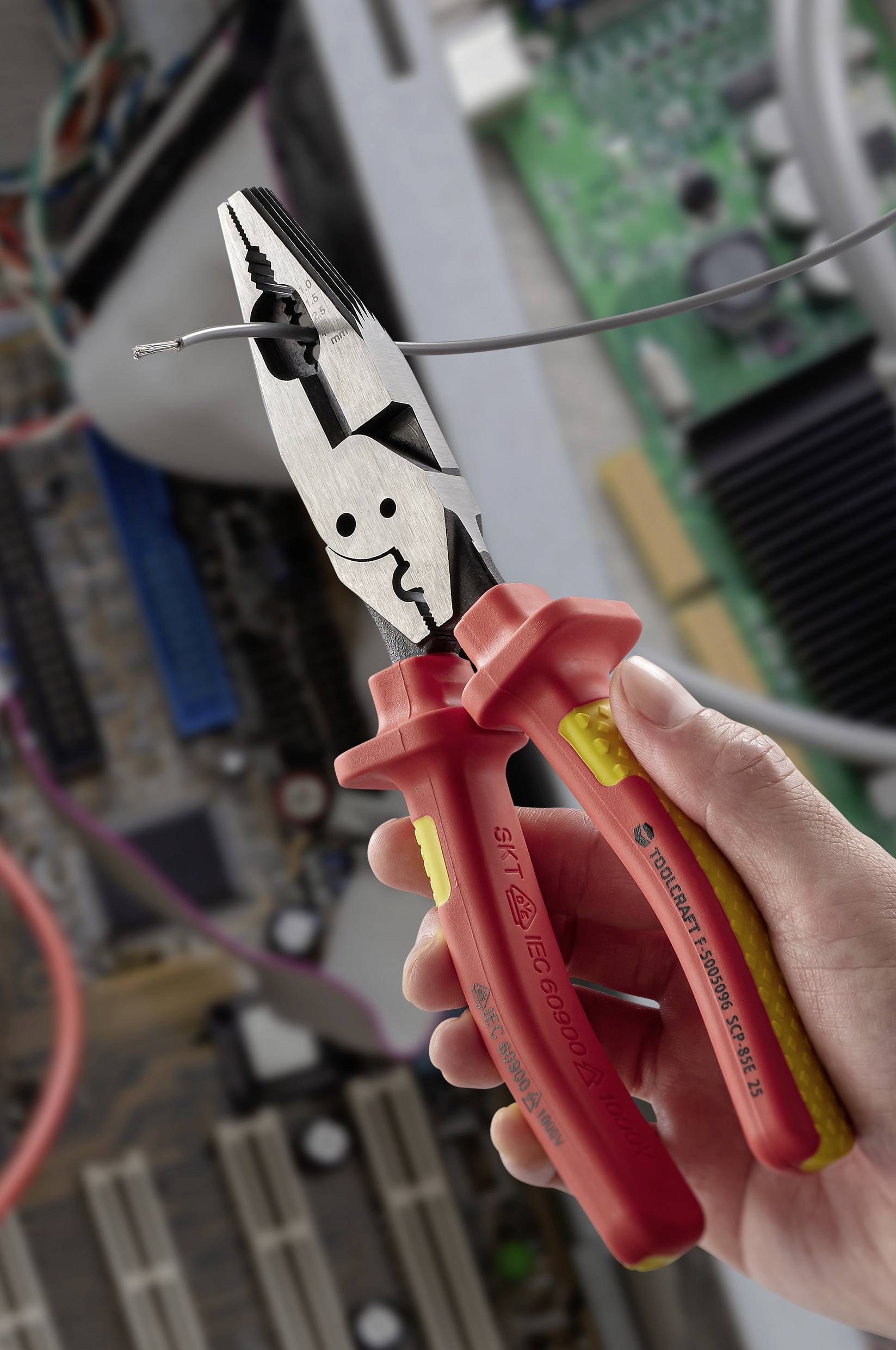 A hand holds red-handled pliers, cutting a wire inside an open computer with visible circuit boards and components.