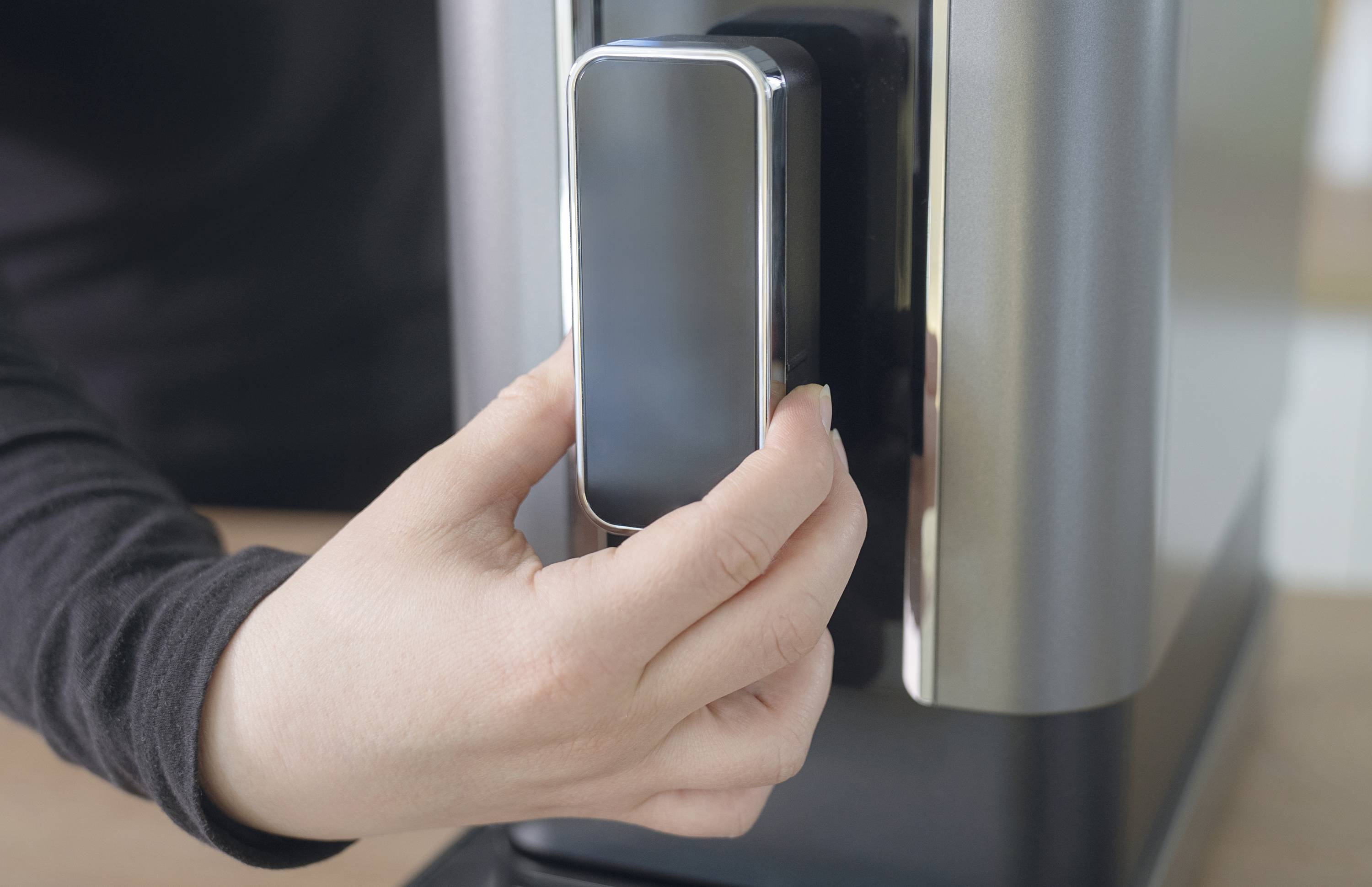 A person is holding a smartphone up to a contactless card reader, presumably to make a payment.