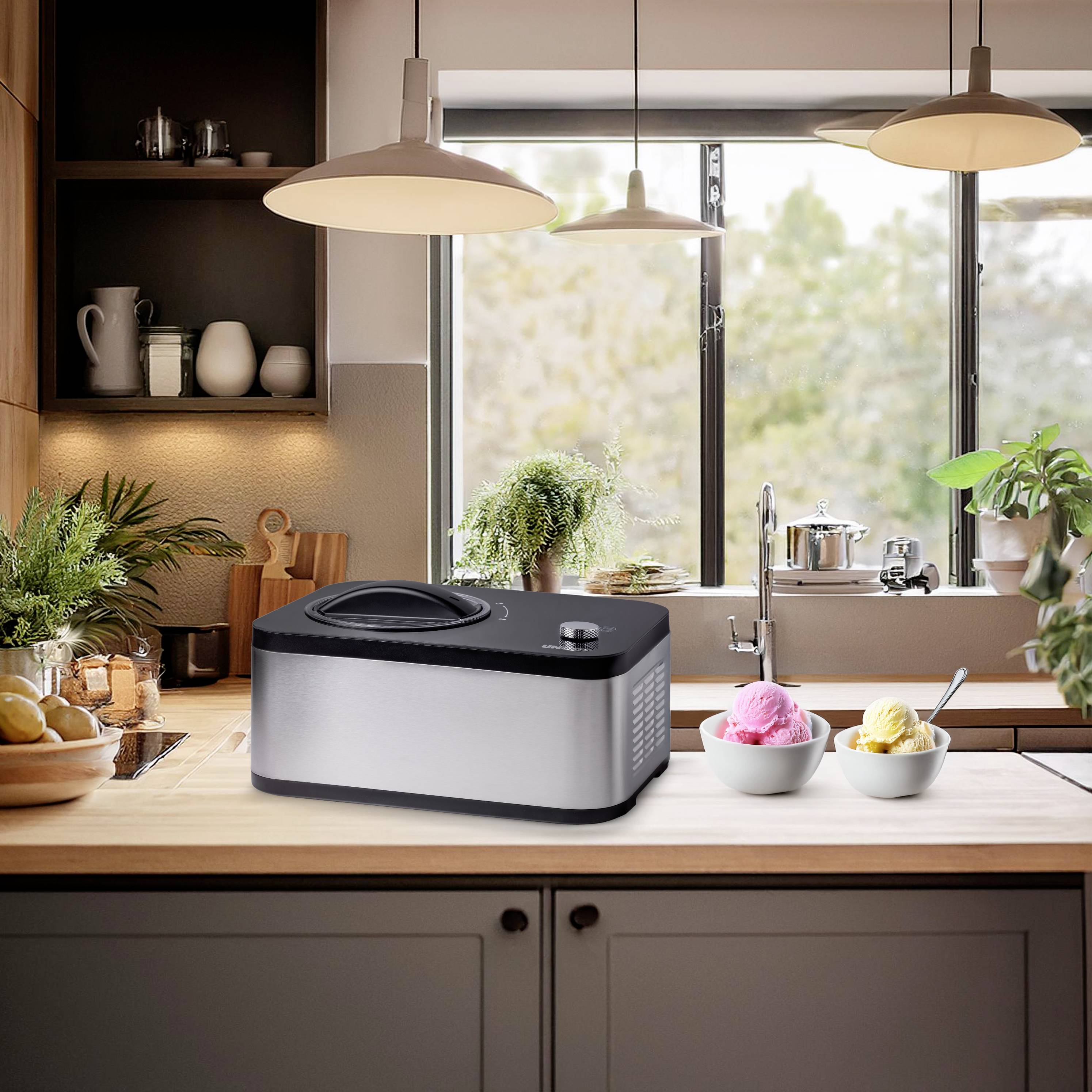 An ice cream maker is standing on the kitchen worktop in front of a window. Beside the machine, three bowls of colourful ice cream are placed.