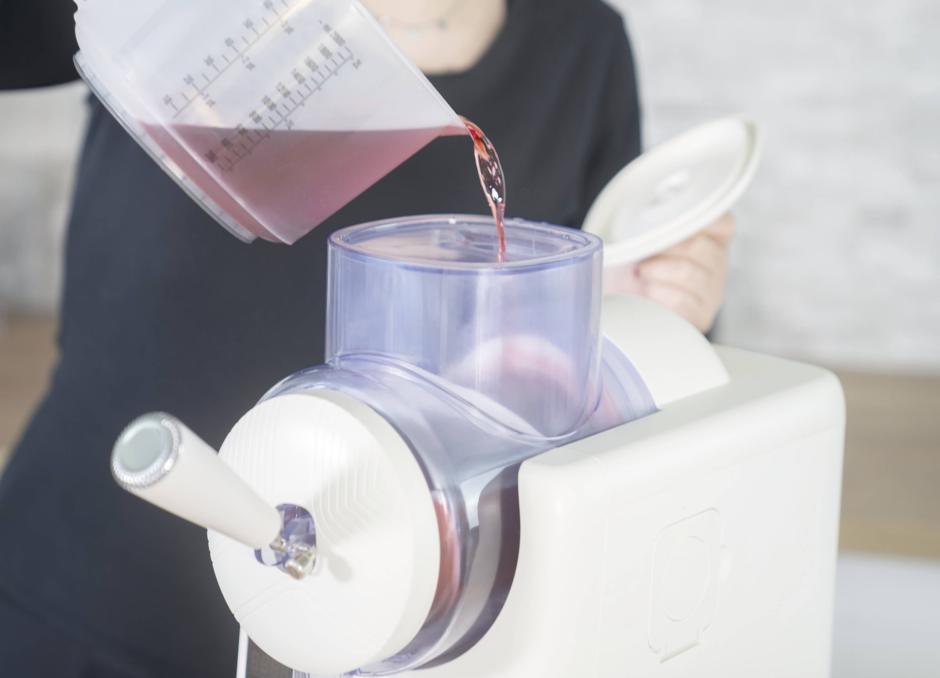 A person is pouring red liquid into a juicer. The juicer has a transparent container.
