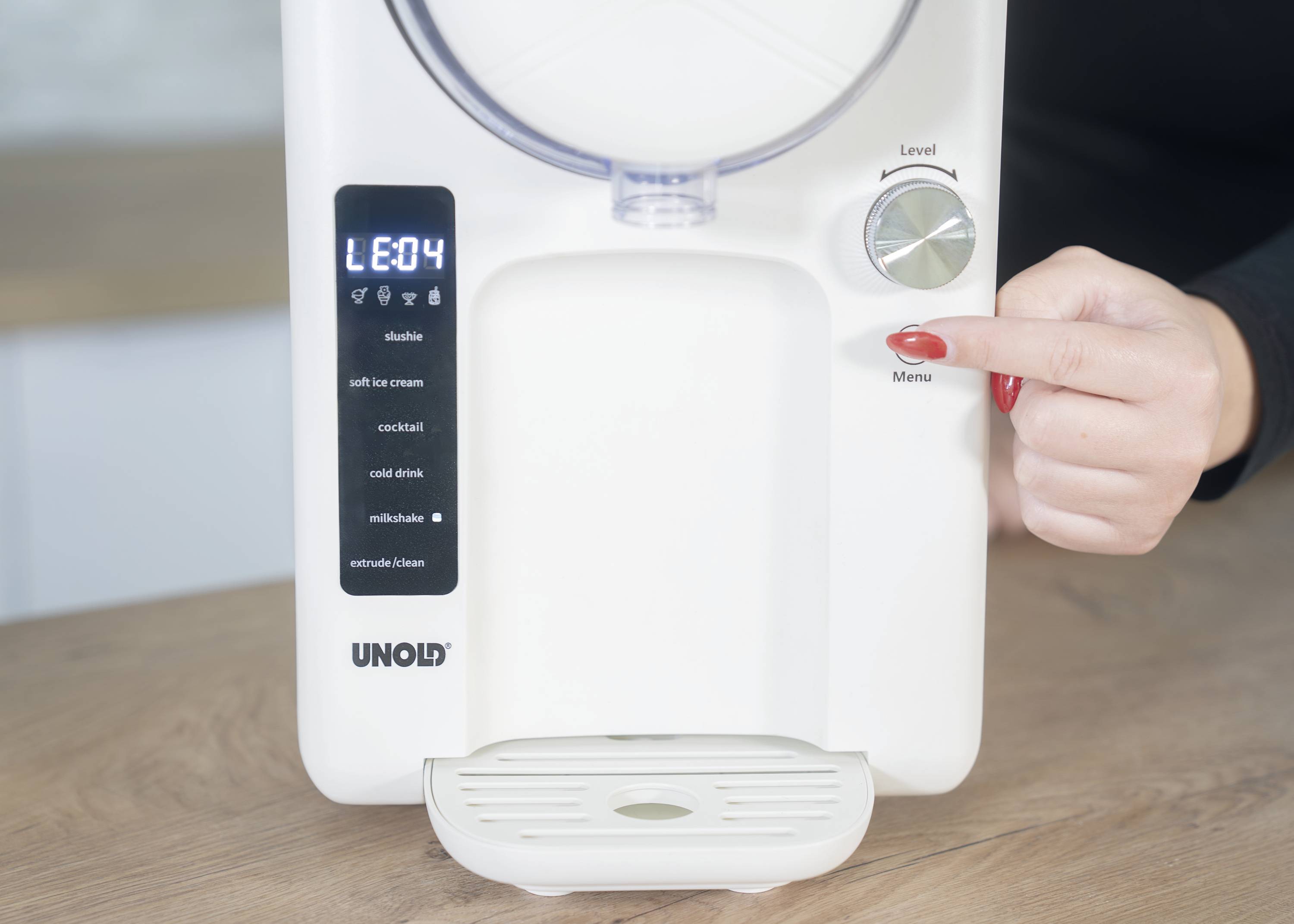 A person operates a white ice cream machine with a digital display. A hand turns the 'Menu' knob to adjust the settings.