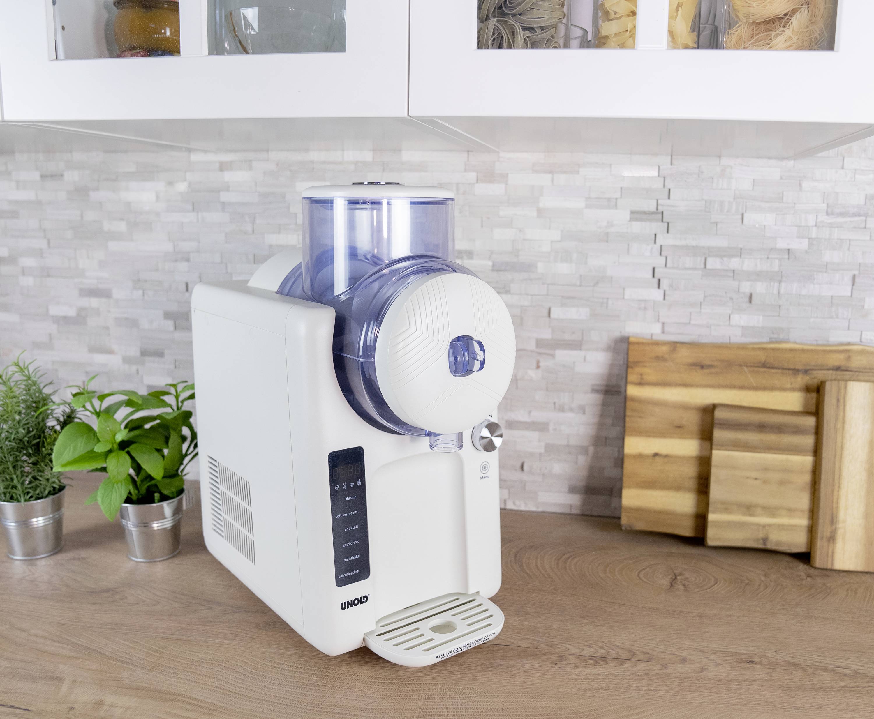 A white stand mixer sits on a wooden worktop. Next to it are potted plants and chopping boards hanging on the wall.
