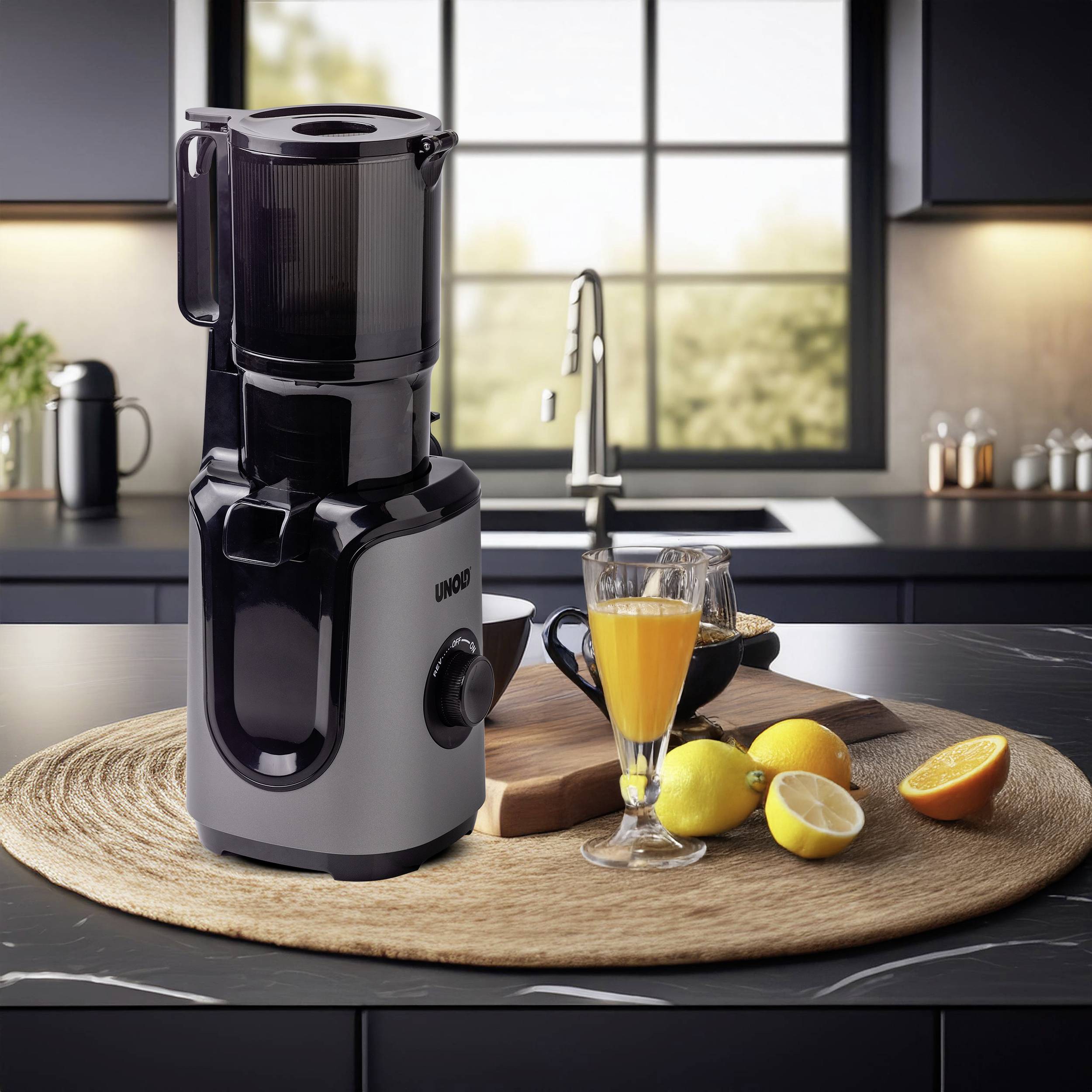 Juicer on a round mat in a kitchen with a glass of freshly squeezed juice, orange slices and lemons, with a blurred window in the background.