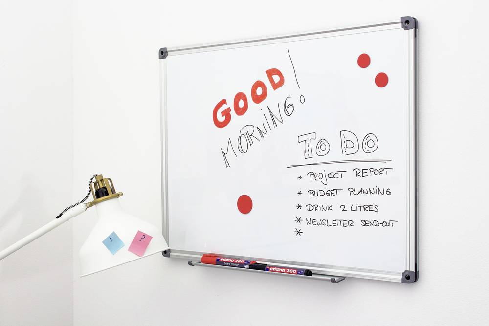 Whiteboard with the inscription 'Good morning! To do: Project report, Budget planning, Drink 2 litres, Newsletter send-out', next to a lamp.