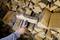 A person is measuring the moisture content of a log using a moisture meter in front of a stack of firewood.