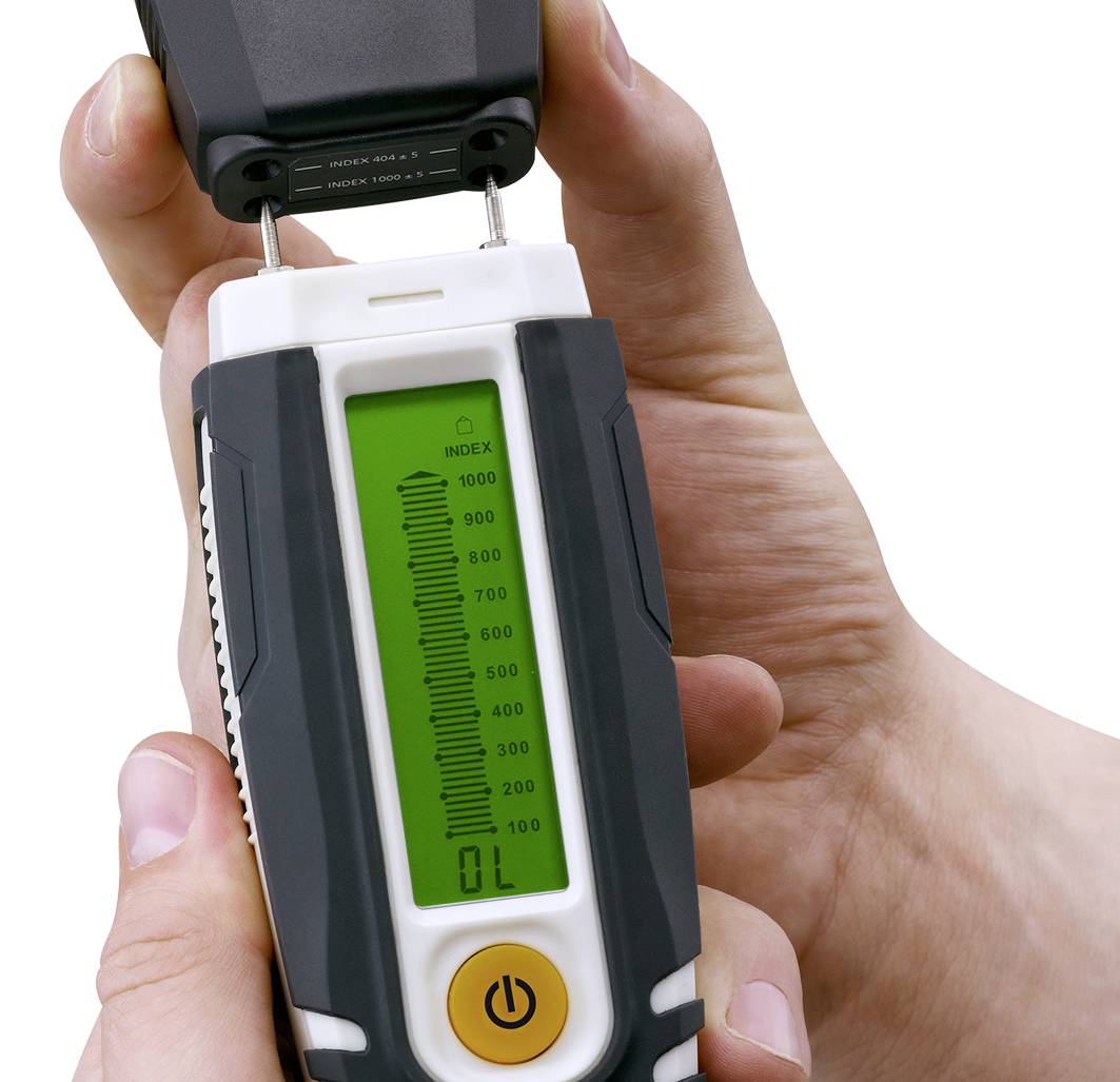 A handheld device for measuring liquids or gases. The scale ranges from 0 to 1000, with the current value standing at 0. Hands are holding the device.