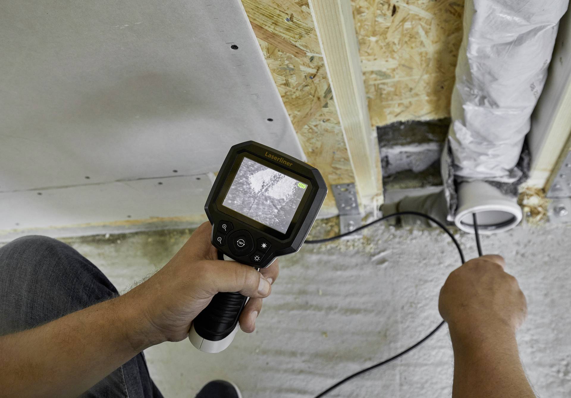 A person is using an inspection camera to check pipes behind a wall. Interior construction site.