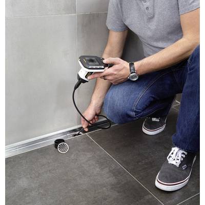 A person is checking a square drainage outlet with an electrical device in a modern bathroom with grey tiles.