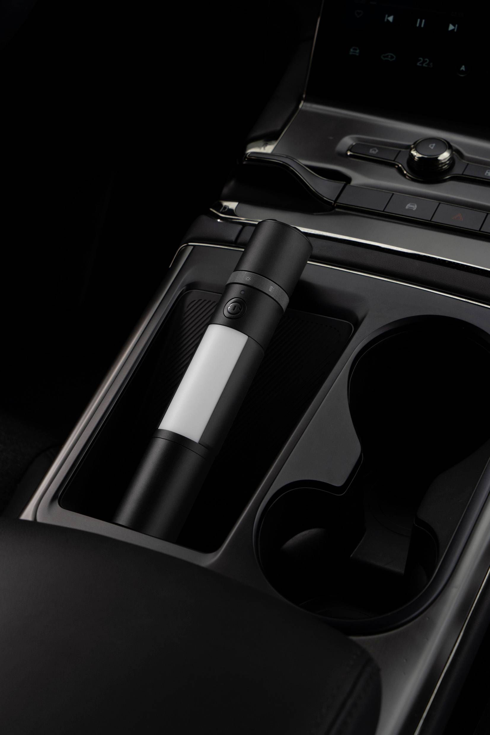 Portable torch placed in the centre console of a car, next to a cup holder.