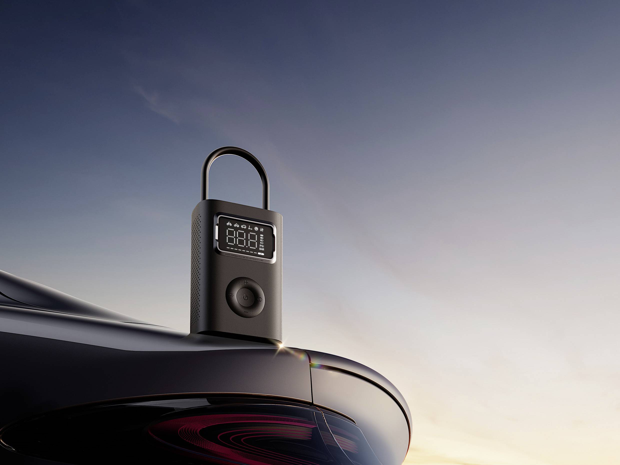 A portable digital tyre air compressor sits on a car roof, against a clear sky at sunset.