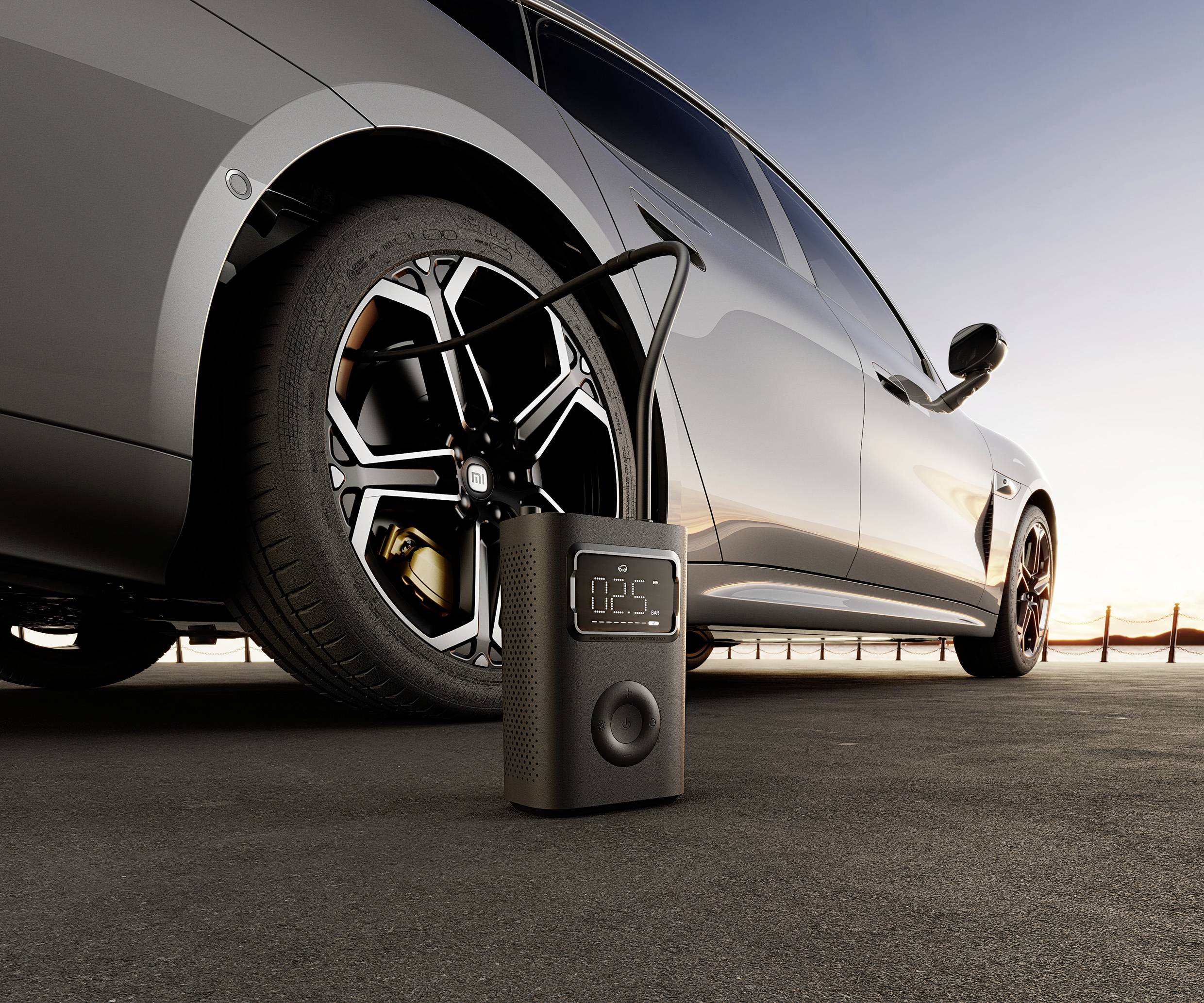 'A car is parked on a car park at sunrise; a portable tyre compressor is connected and shows 2.5 bar.'