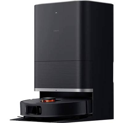 A black robotic vacuum cleaner in a charging station. The robot has an orange marking on its top surface and is ready for cleaning.