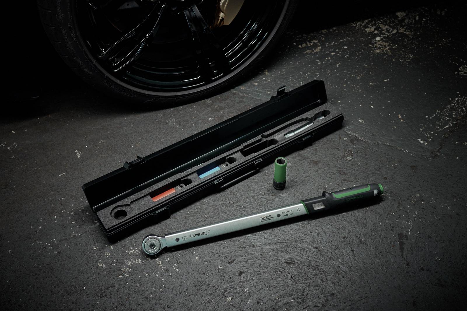 Torque wrench and sockets on concrete floor beside tyre. Tool protective case open in the background.