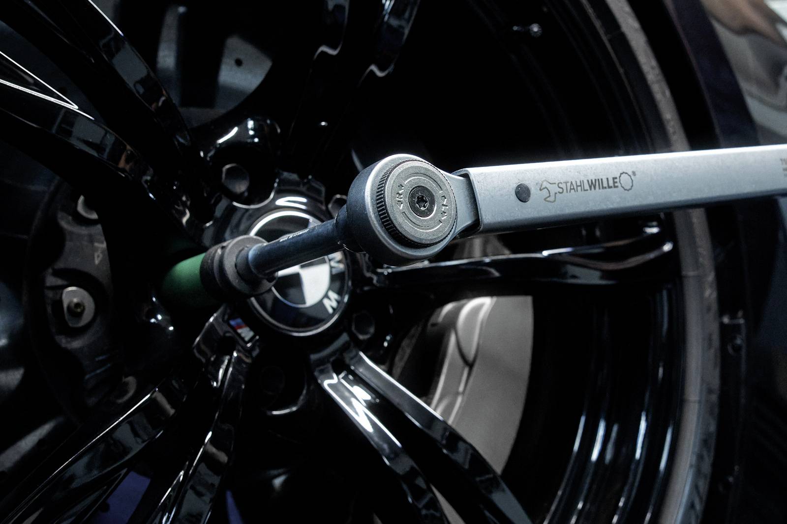 A torque wrench is tightening a wheel nut on a black car tyre using a hexagonal adapter.