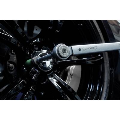A torque wrench is tightening a wheel nut on a black car tyre using a hexagonal adapter.