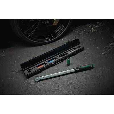A torque wrench lies on a workshop floor next to its open case and a socket, in front of a car tyre.