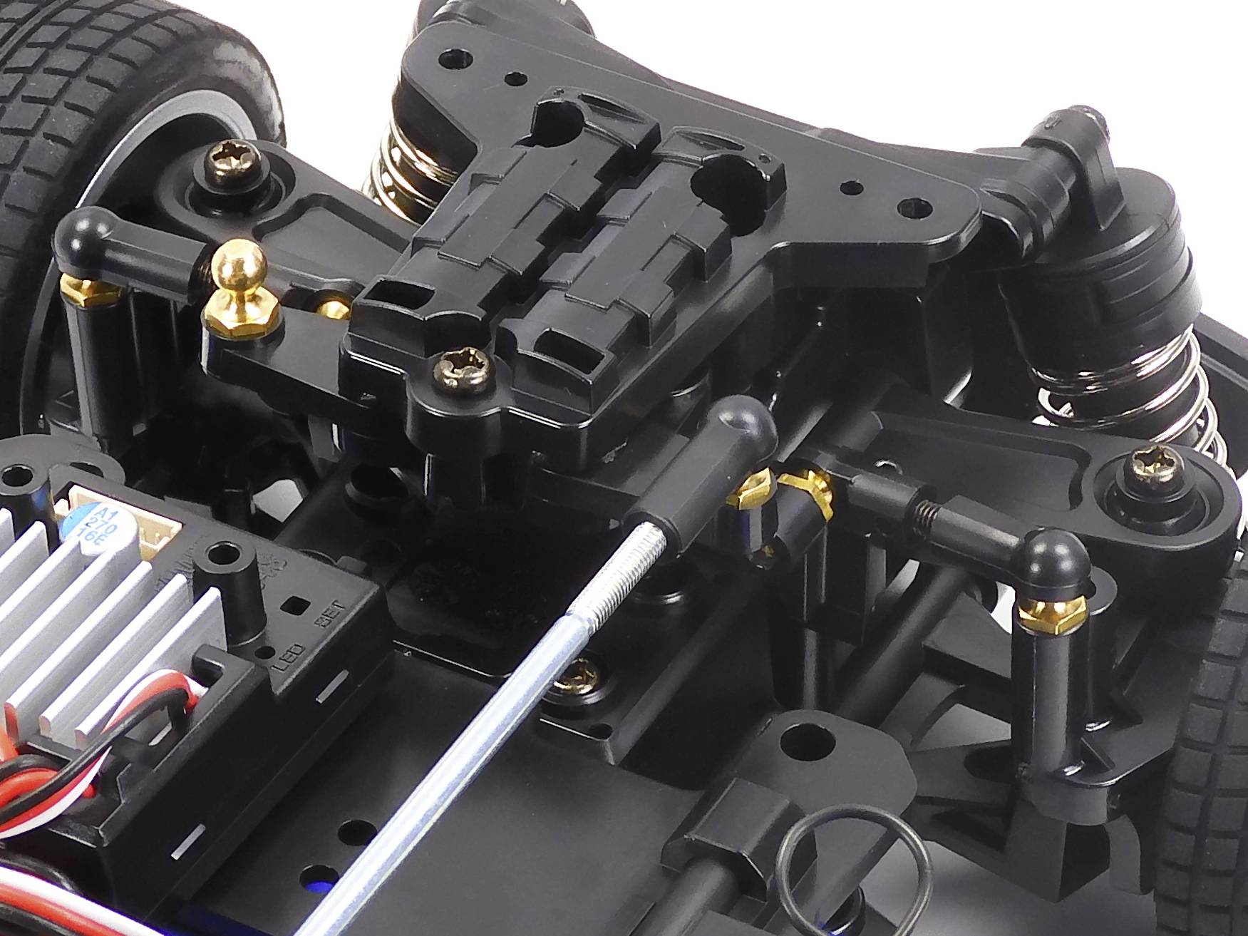 Close-up of a remote-controlled model car chassis with visible shock absorbers, cables, and drive components.