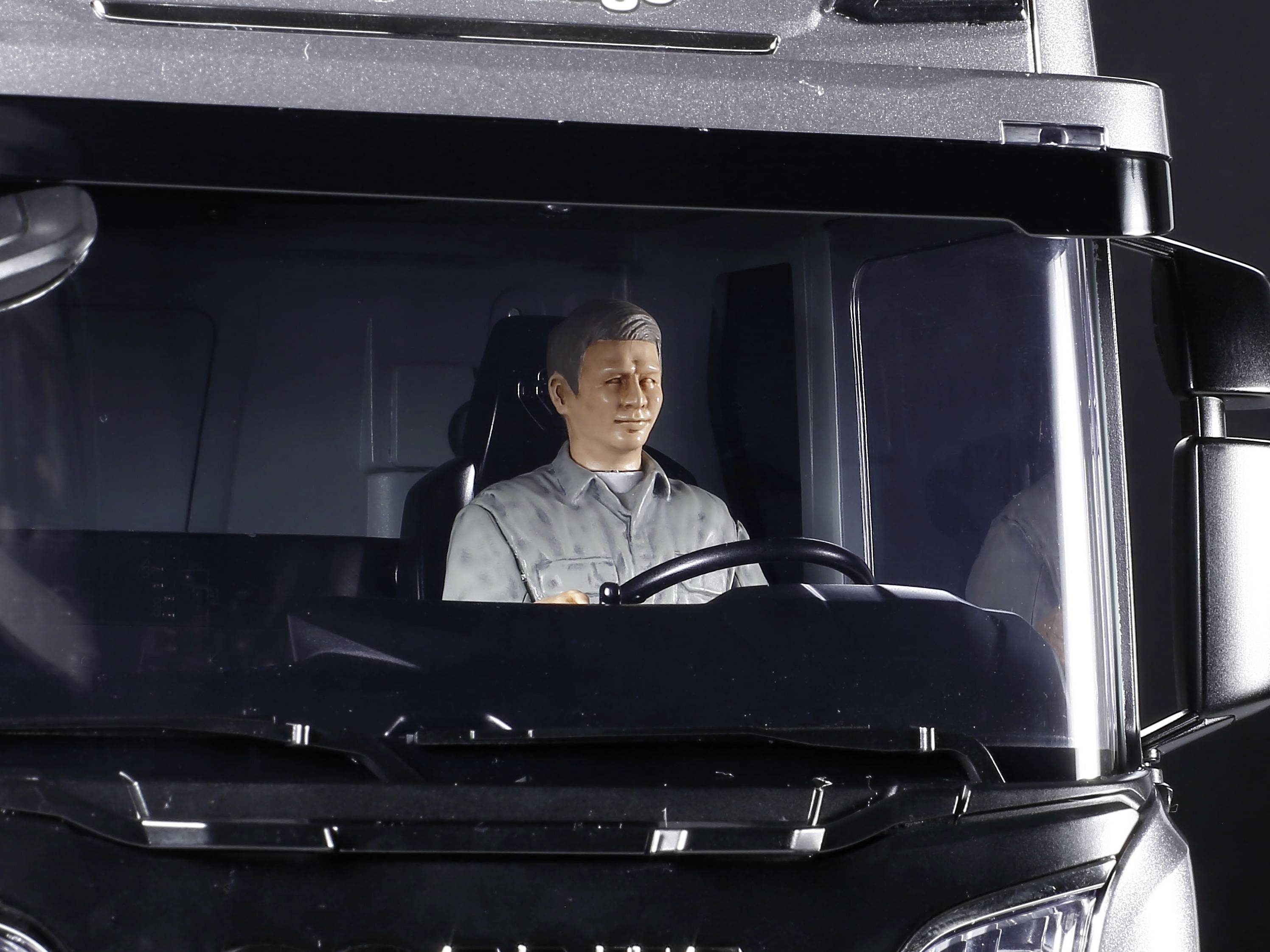 A male figure sits at the steering wheel of a model vehicle, looking straight ahead.