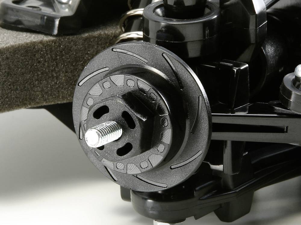 Close-up of a black RC car wheel system with brake disc and suspension. Detailed mechanics visible.