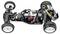 Remote-controlled car chassis with exposed electronics, studded tyres, suspension, and visible cables.