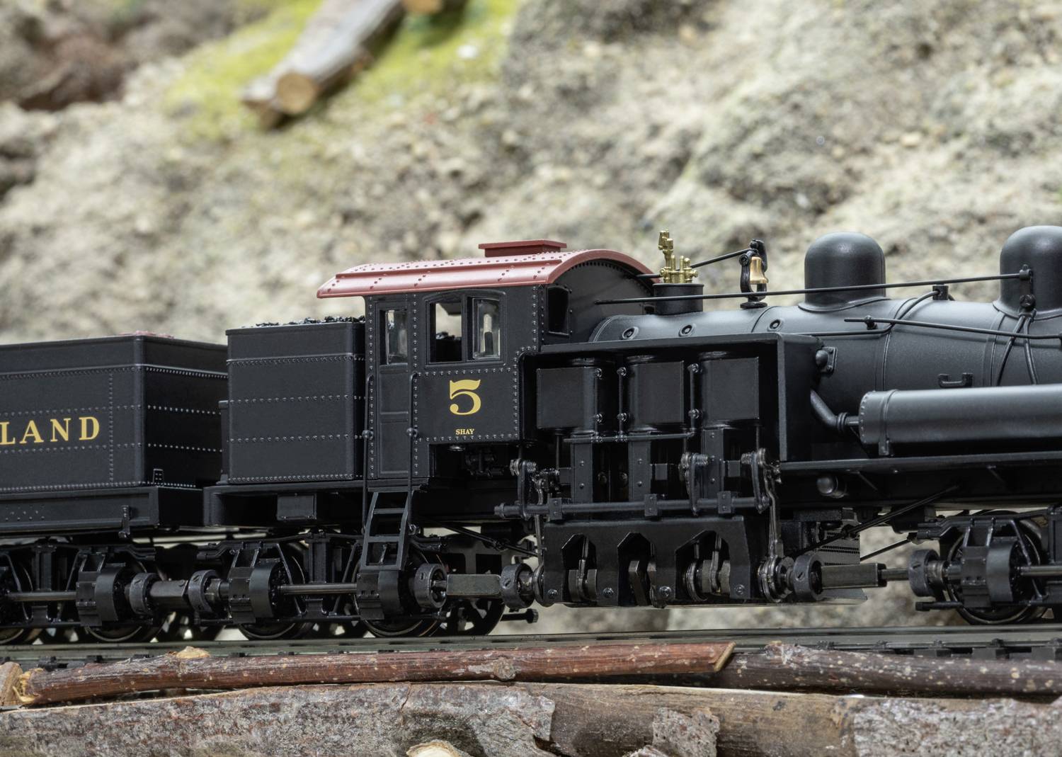 Model railway in landscape diorama. The locomotive is black with the number '5' and is pulling a wagon with the inscription 'LAND'.