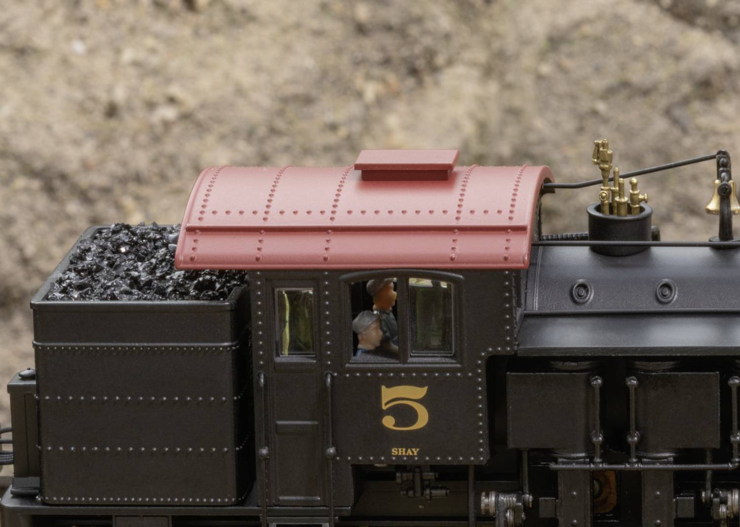 A detailed model railway steam locomotive of the Shay type with a red roof and coal wagon, photographed from the side, with a driver visible in the window.