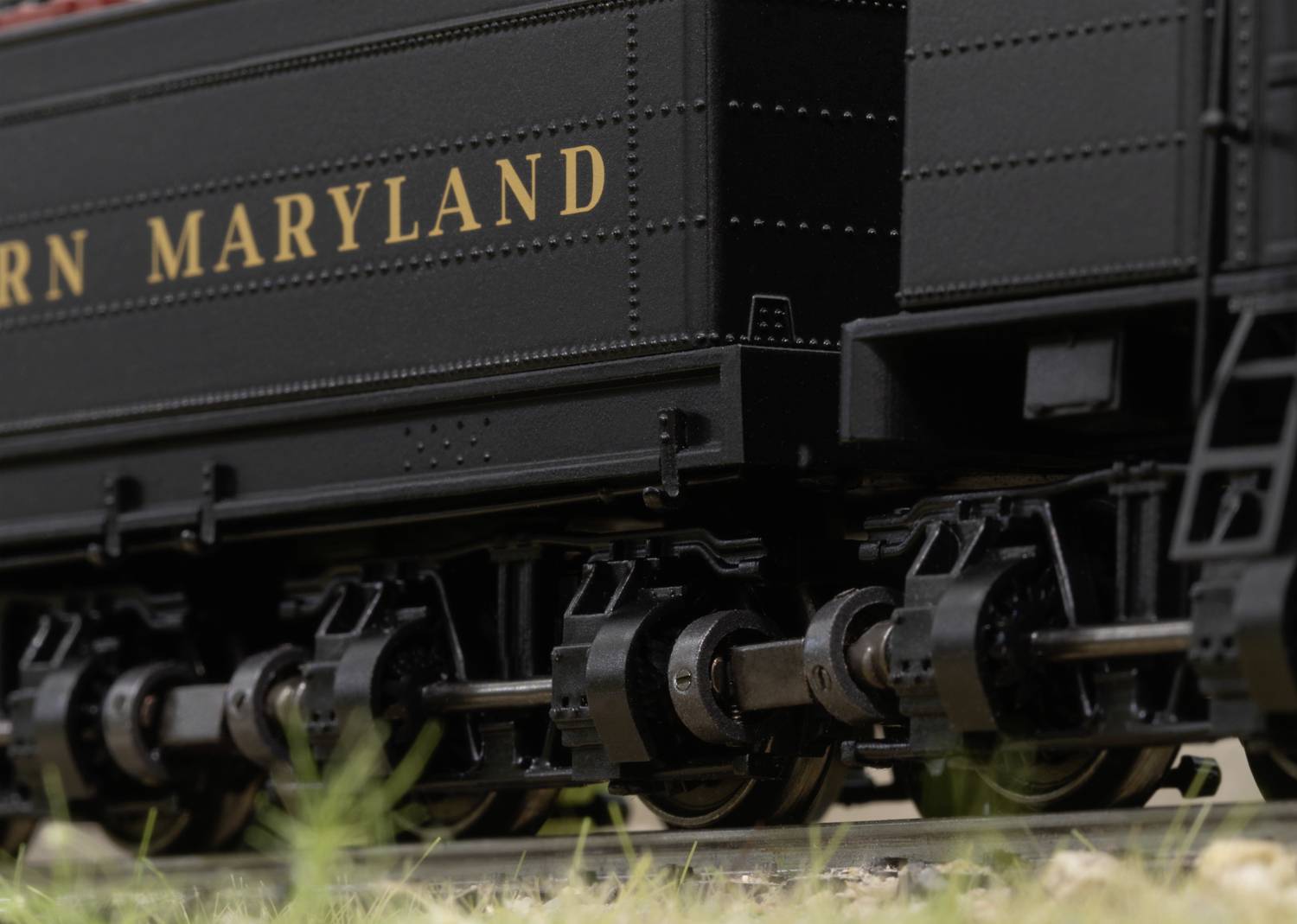 Close-up of railway wheels on tracks. The wagon highlights 'Western Maryland'. Grasses are growing near the railway lines.