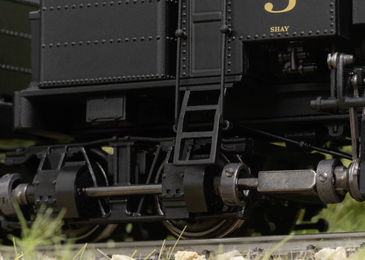 Close-up of a black steam locomotive chassis with visible wheels and mechanisms on an outdoor section of railway track.