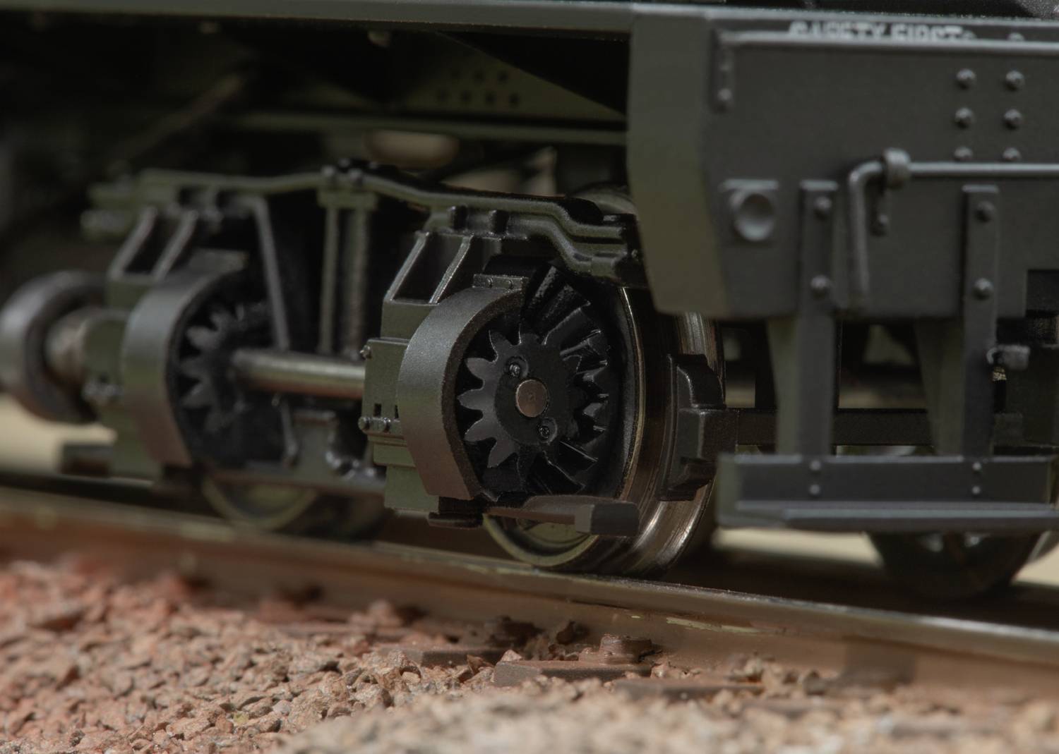 Close-up of a train bogie on rails, showing a detailed view of the wheels and suspension on a ballast bed.