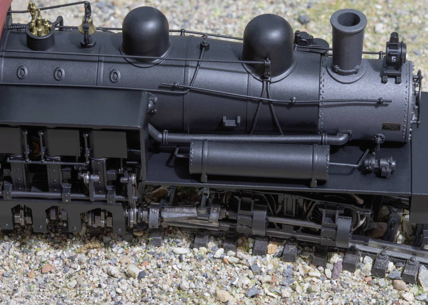 A detailed model of a black steam locomotive, positioned on a track with gravel and small stones in the background.