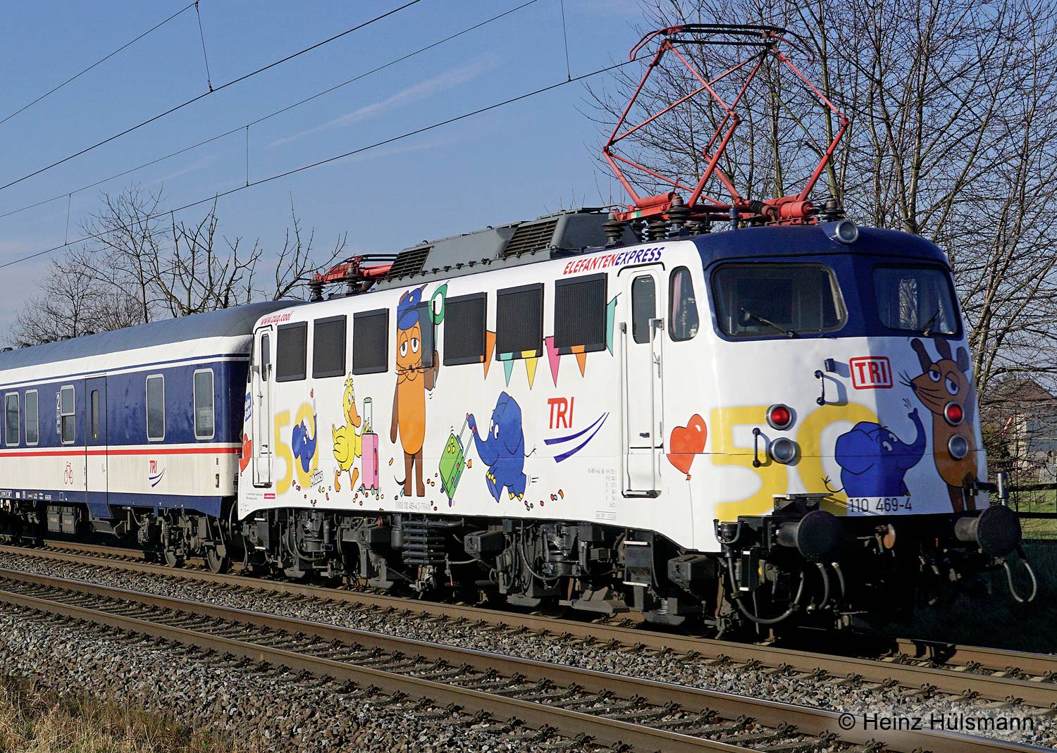 A colourful train with cartoon graphics travels along a railway line. It is a Europa Express with decorations and an electric locomotive.