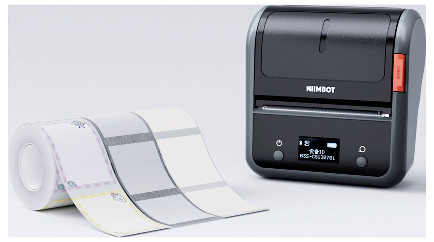 A small, black label printer next to a roll of printable labels. The printer displays a digital screen.
