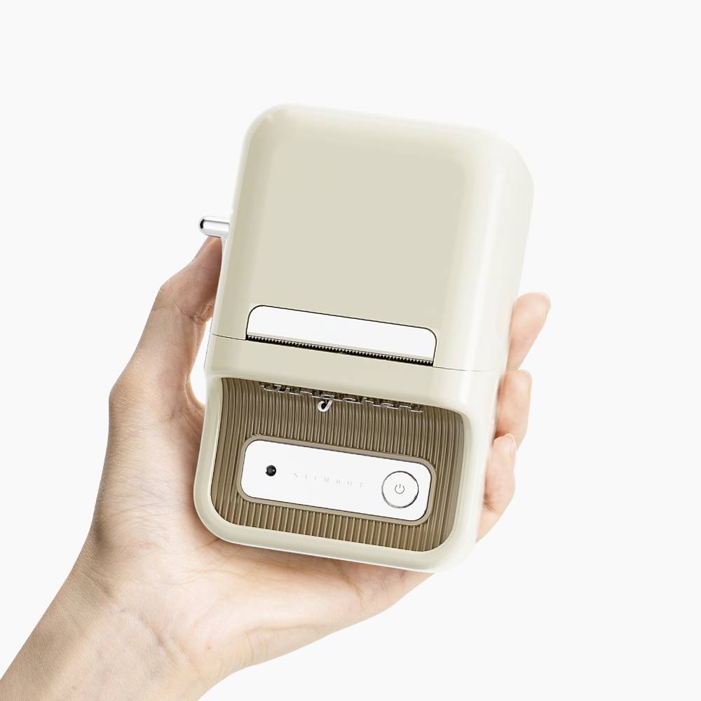 A hand is holding a small, beige electronic device box with a button and a flap, suitable for storing small objects.
