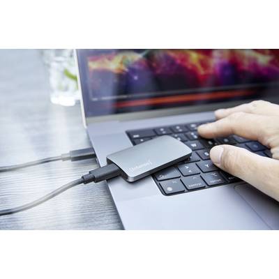 A hand is typing on a laptop keyboard. An external drive is connected to the laptop via a cable.