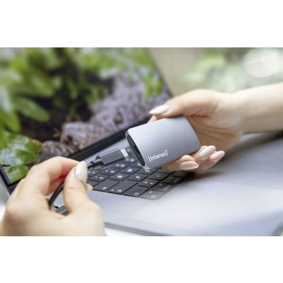 A person is holding an external hard drive in front of a laptop, ready to connect it with a USB cable.