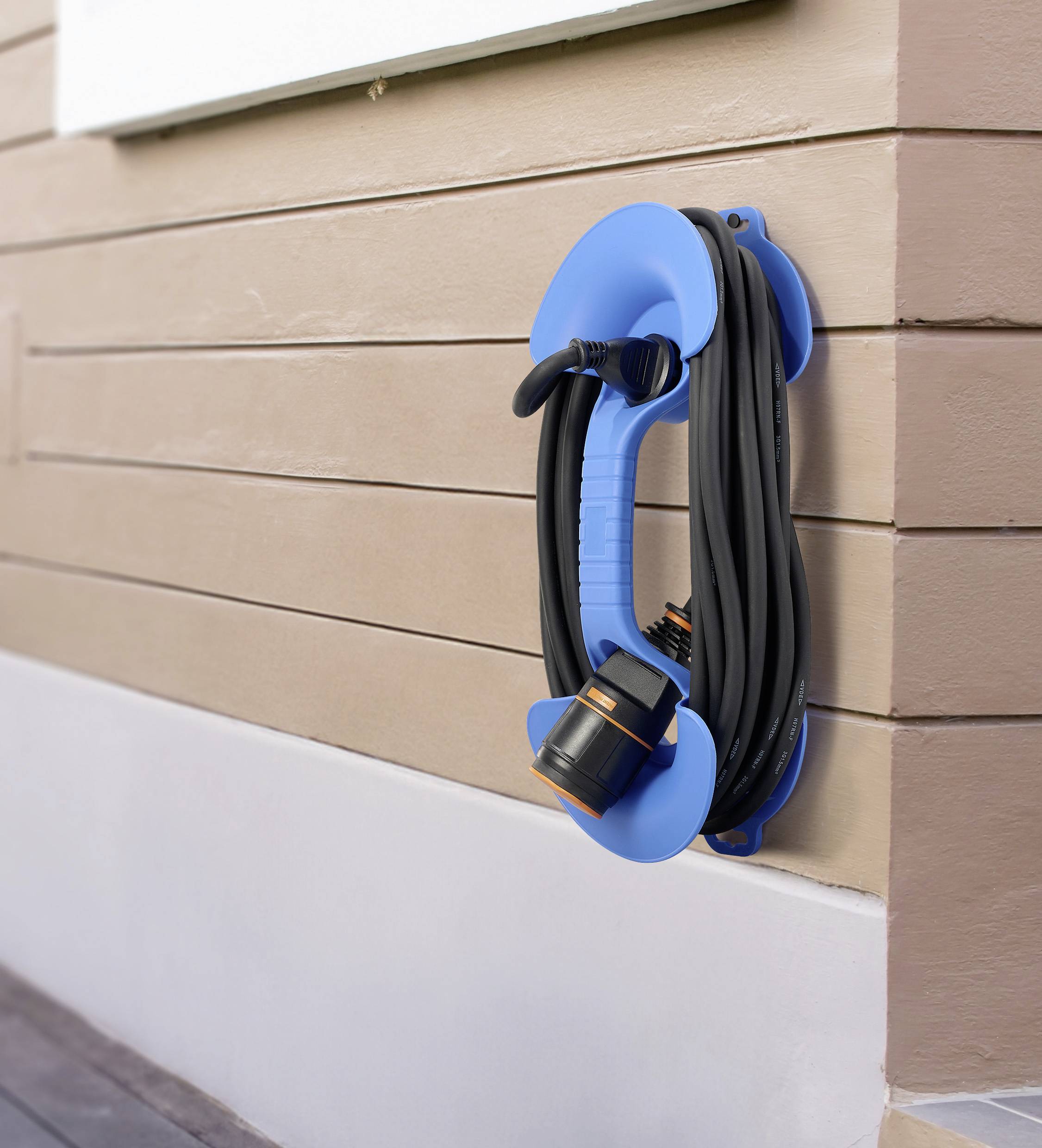 A garden hose is neatly coiled on a blue holder attached to the wall of a house.