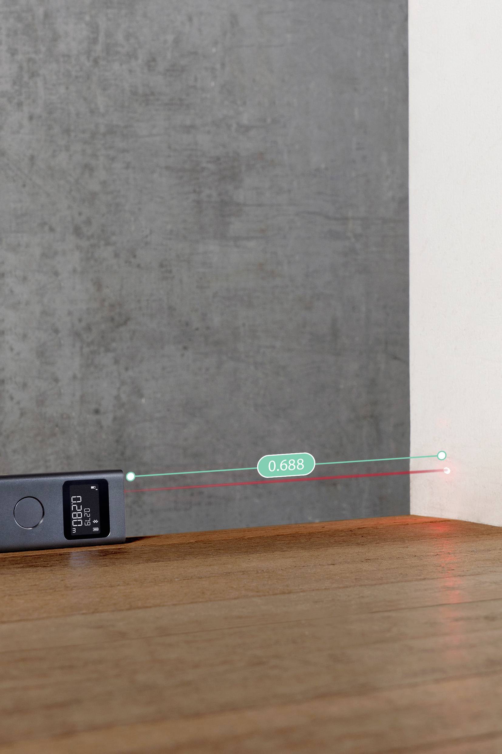 'A digital laser distance meter measures the distance from a wooden surface to a wall, displaying a reading of 0.688 on its screen.'