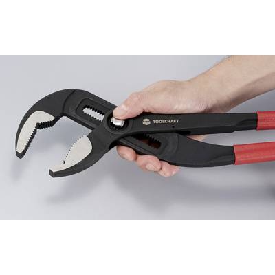 A person holds a pair of adjustable pliers with red handles, showing its open jaws and serrated gripping surfaces, against a light gray background.