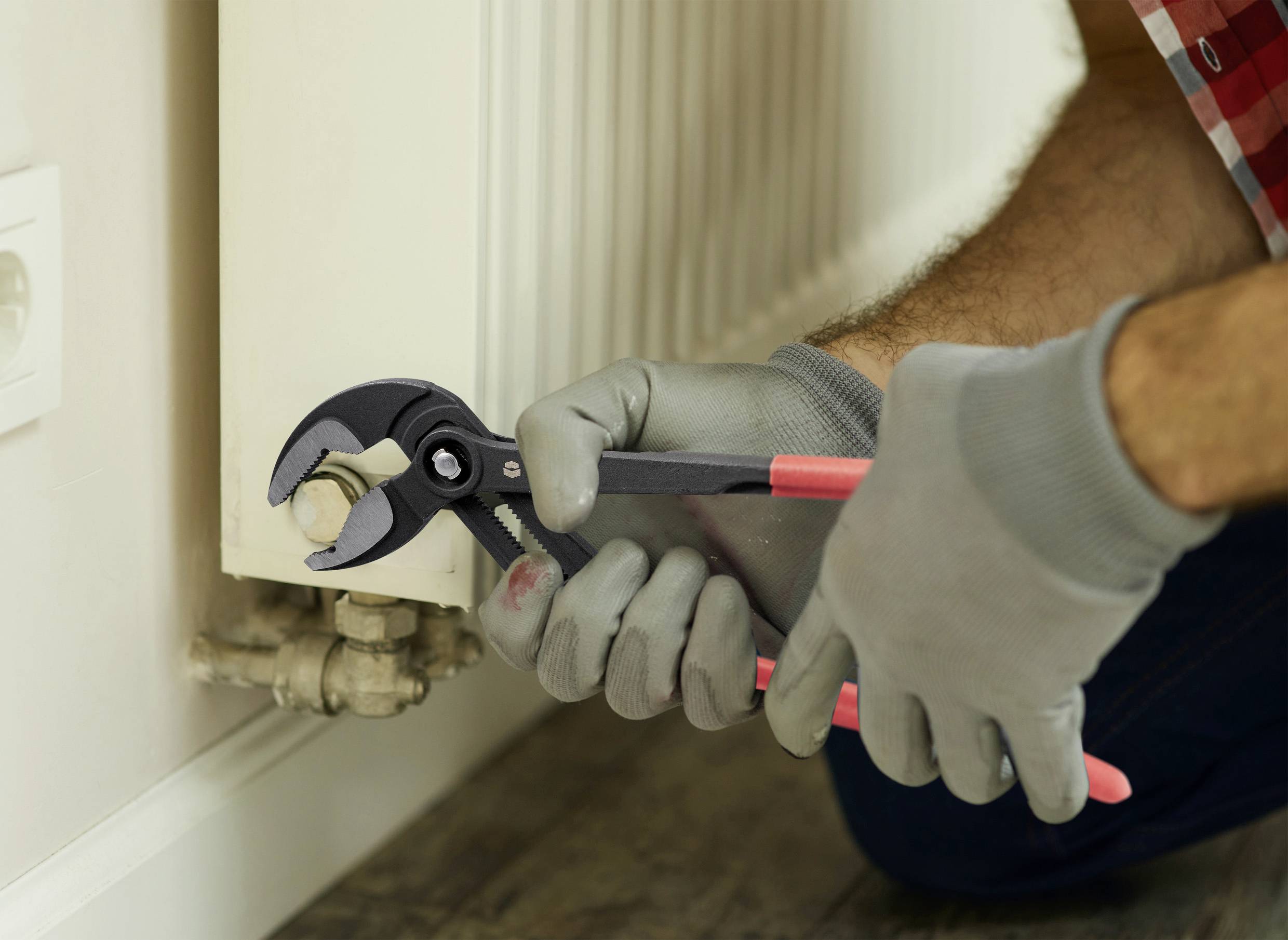 A person wearing gloves uses pliers to adjust a valve on a radiator.