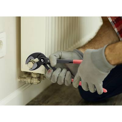 A person wearing gloves uses pliers to adjust a valve on a radiator.