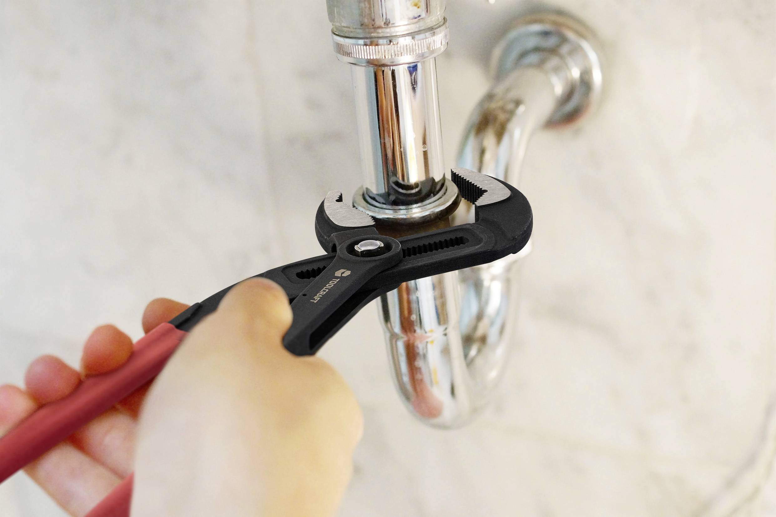 A person uses a wrench to tighten a pipe under a sink, indicating plumbing maintenance.
