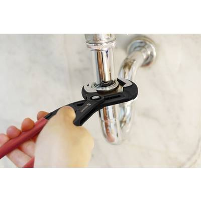 A person uses a wrench to tighten a pipe under a sink, indicating plumbing maintenance.