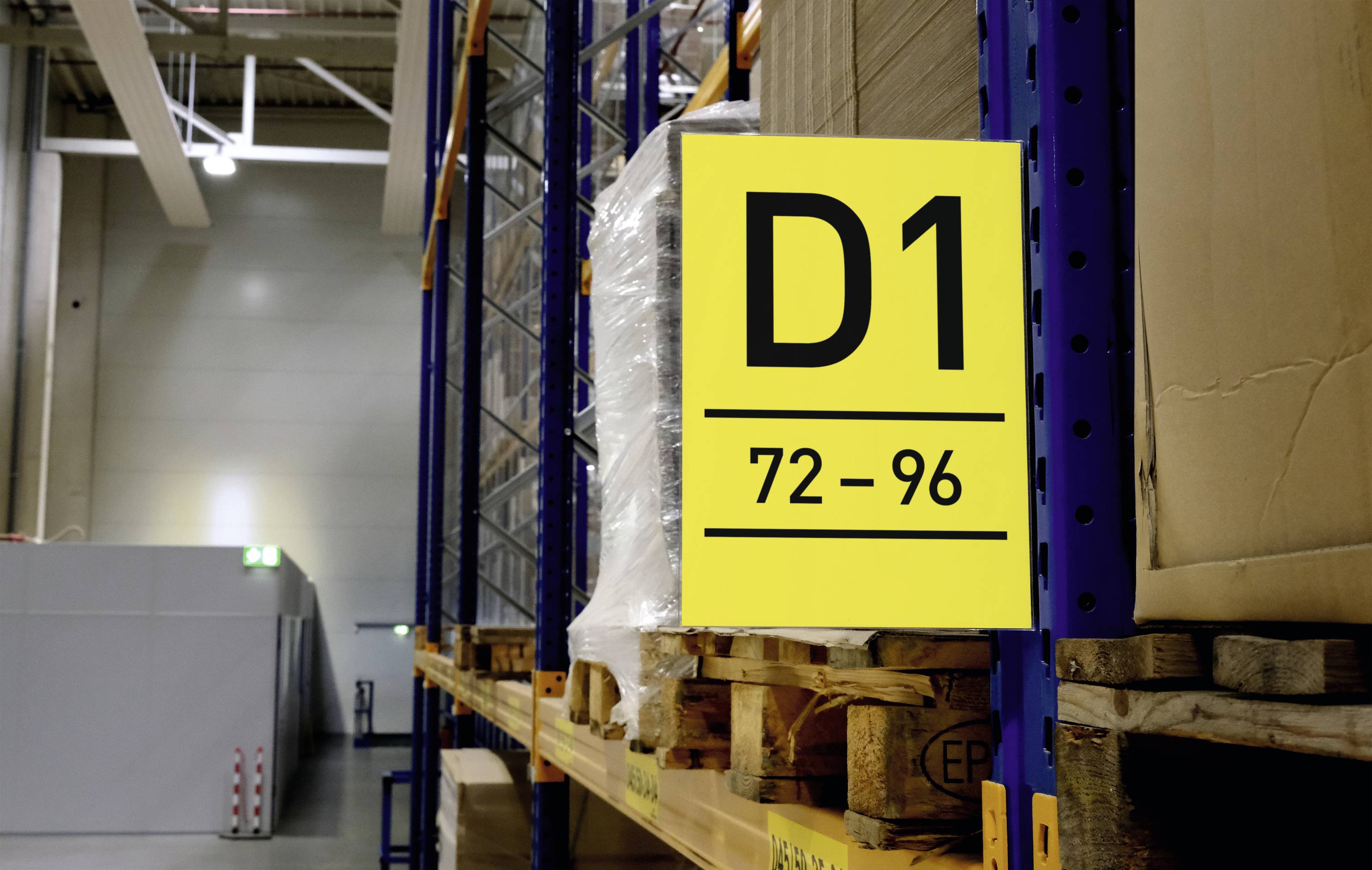Yellow sign with the inscription 'D1 72-96' is hanging on a shelf in a warehouse. Pallets are stacked underneath.